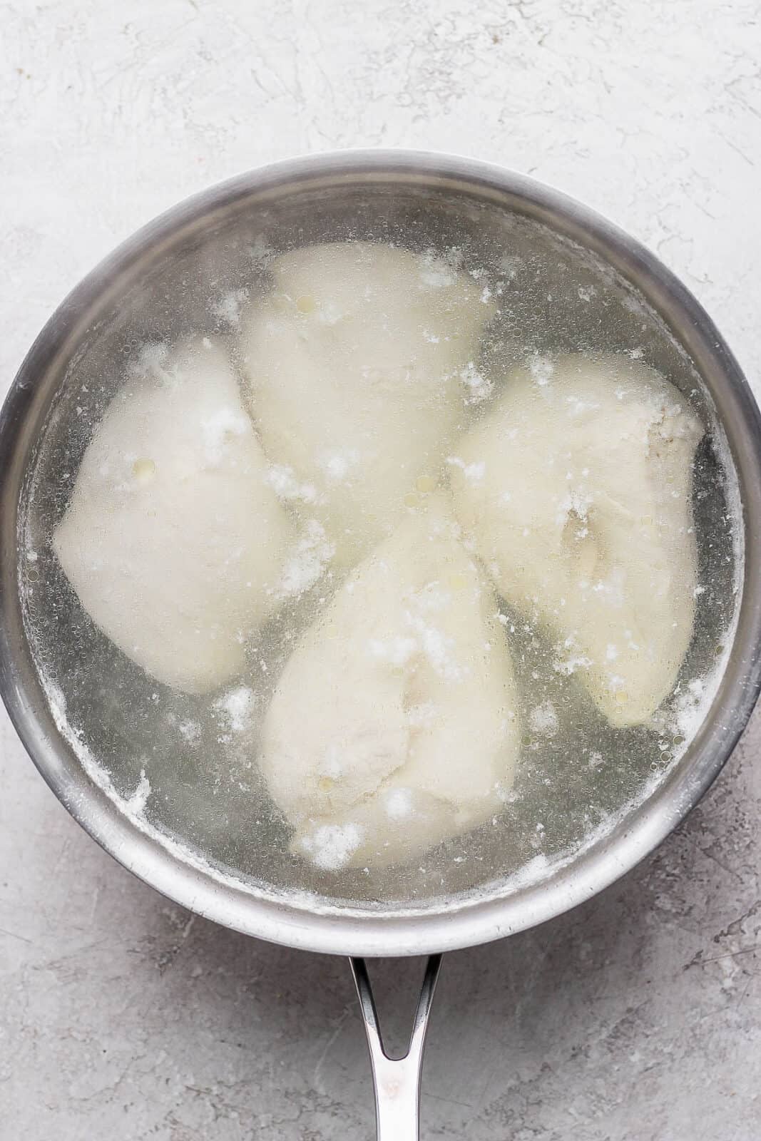 A large pot of water with three chicken breast that has been boiled.