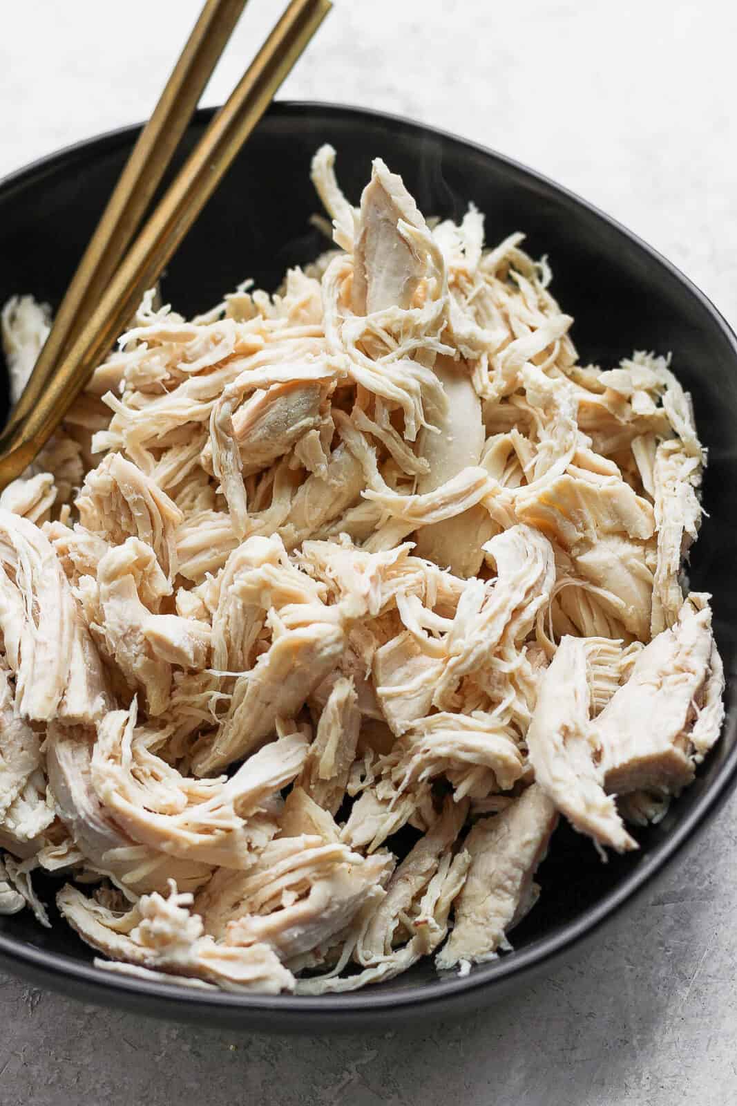 Shredded poached chicken in a black blow with two gold forks.