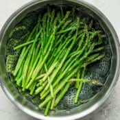 Asparagus being steamed in a saucepan with steamer basket.