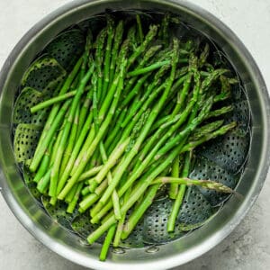 Asparagus being steamed in a saucepan with steamer basket.