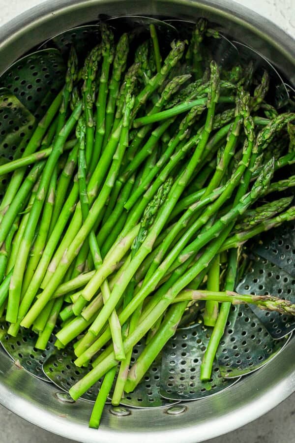 Asparagus being steamed in a saucepan with steamer basket.