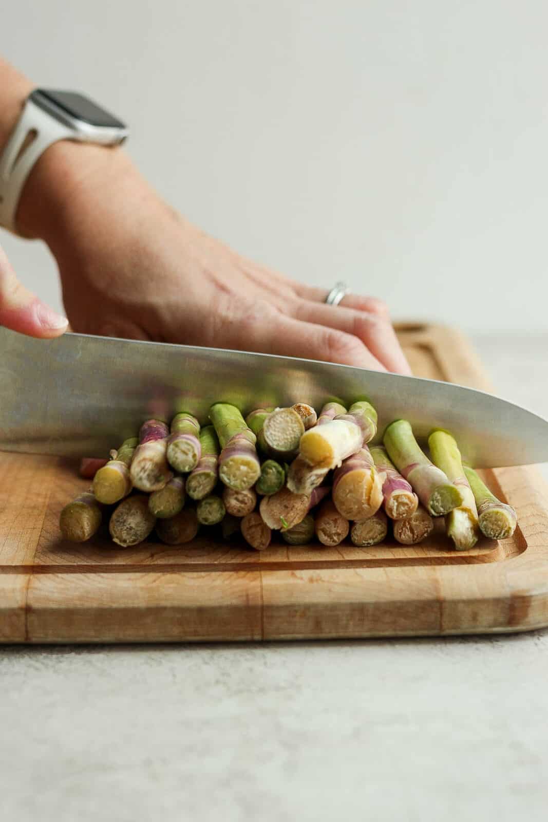 Asparagus on a cutting board with the ends being trimmed off.