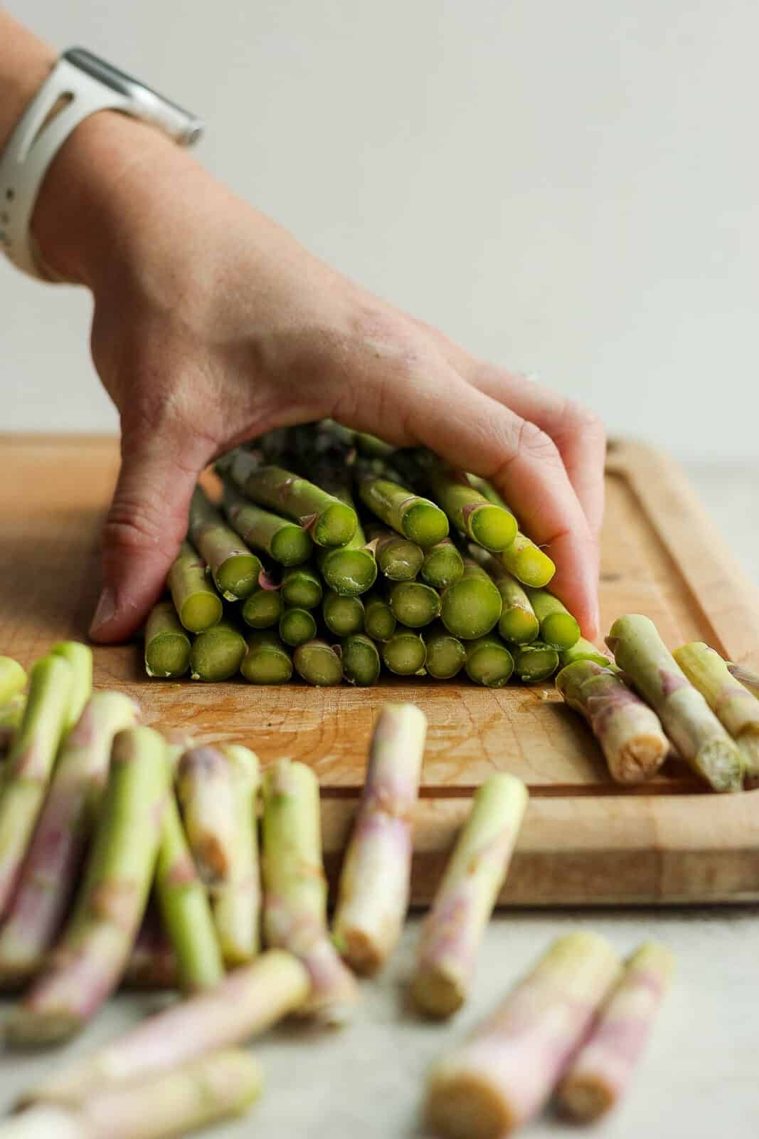 A hand holding a bunch of asparagus on a cutting board after the ends were trimmed off.