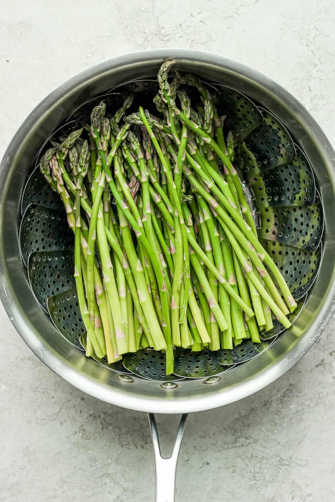 Asparagus stalks in the steamer basket in a pot.