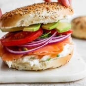 A fully assembled lox bagel on a white marble board.