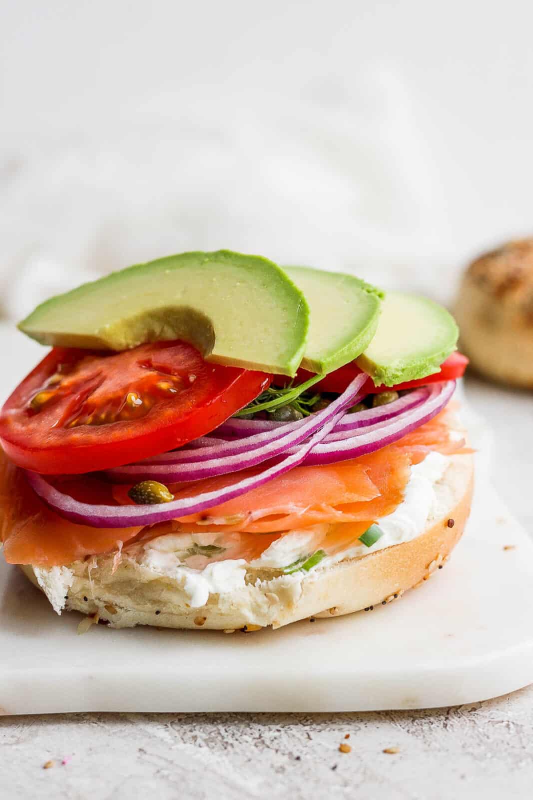 A lox bagel with tomato and avocado slices added on top.