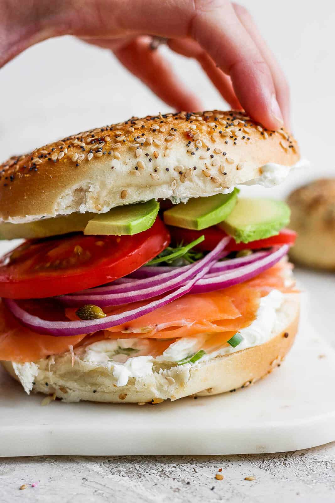 A hand placing the top half of the bagel on an ultimate lox bagel.