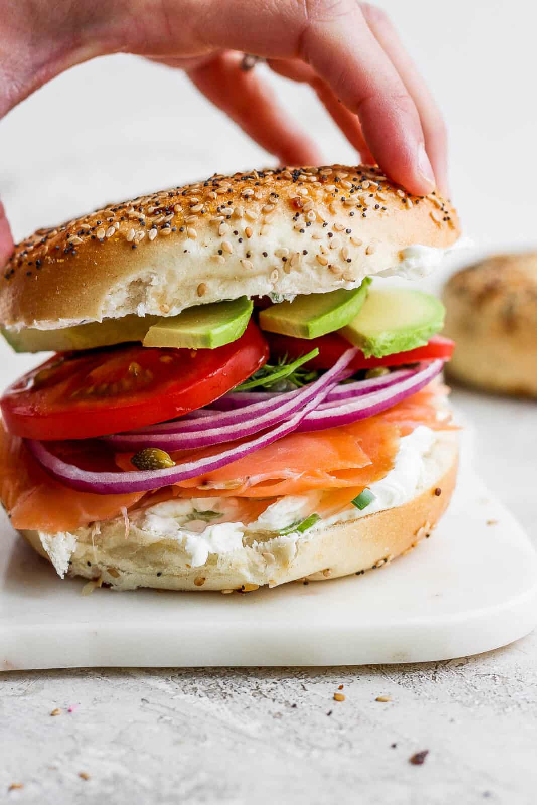 A hand placing the top bagel on an ultimate lox bagel.