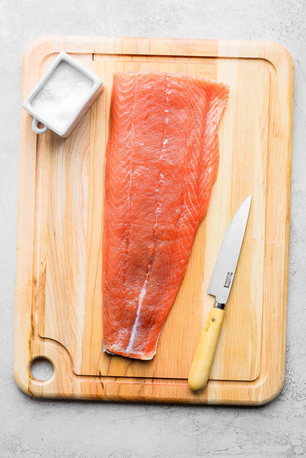 A cutting board with lox, salt, and a knife.