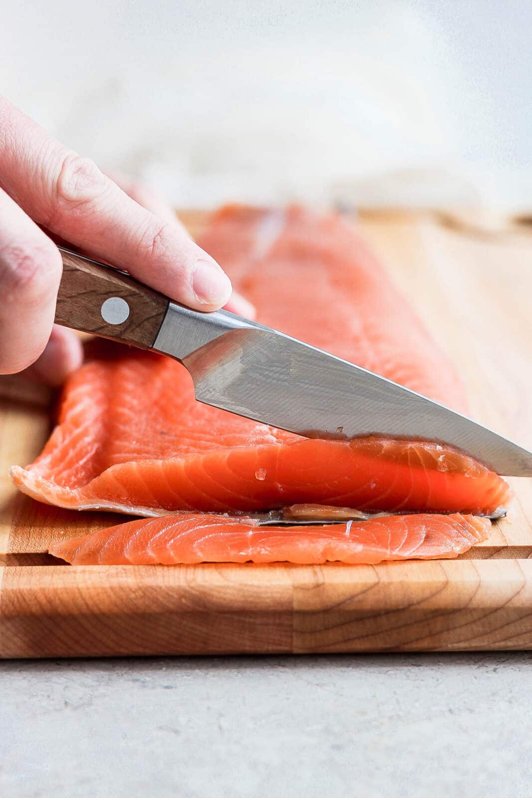 A large piece of lox being cut into very thin slices.