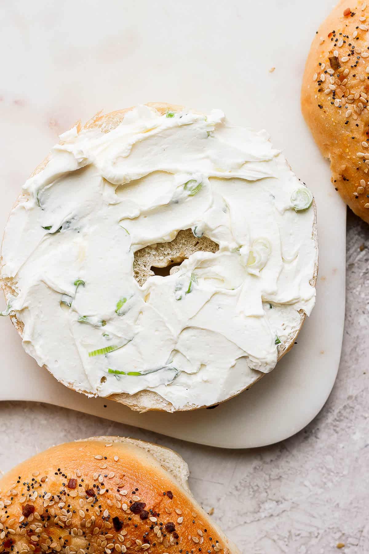 Scallion cream cheese spread on the bottom half of a bagel.