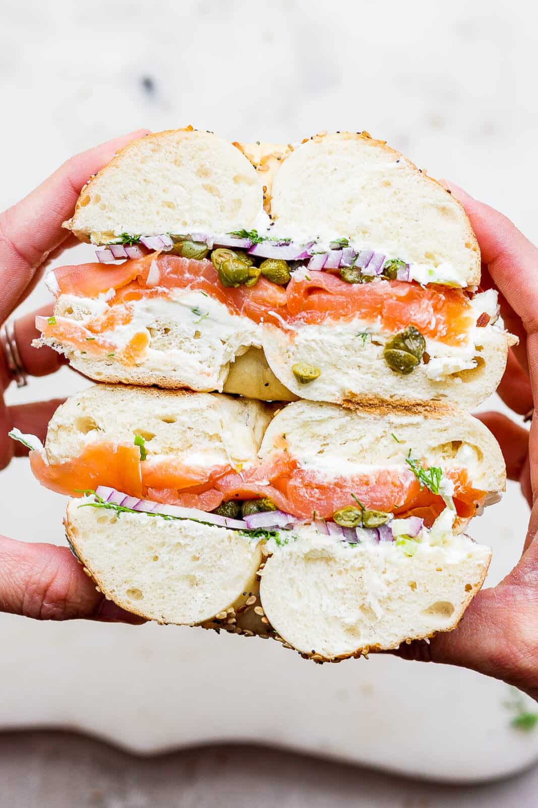 A lox bagel sandwich cut in half and held so you can see the inside.