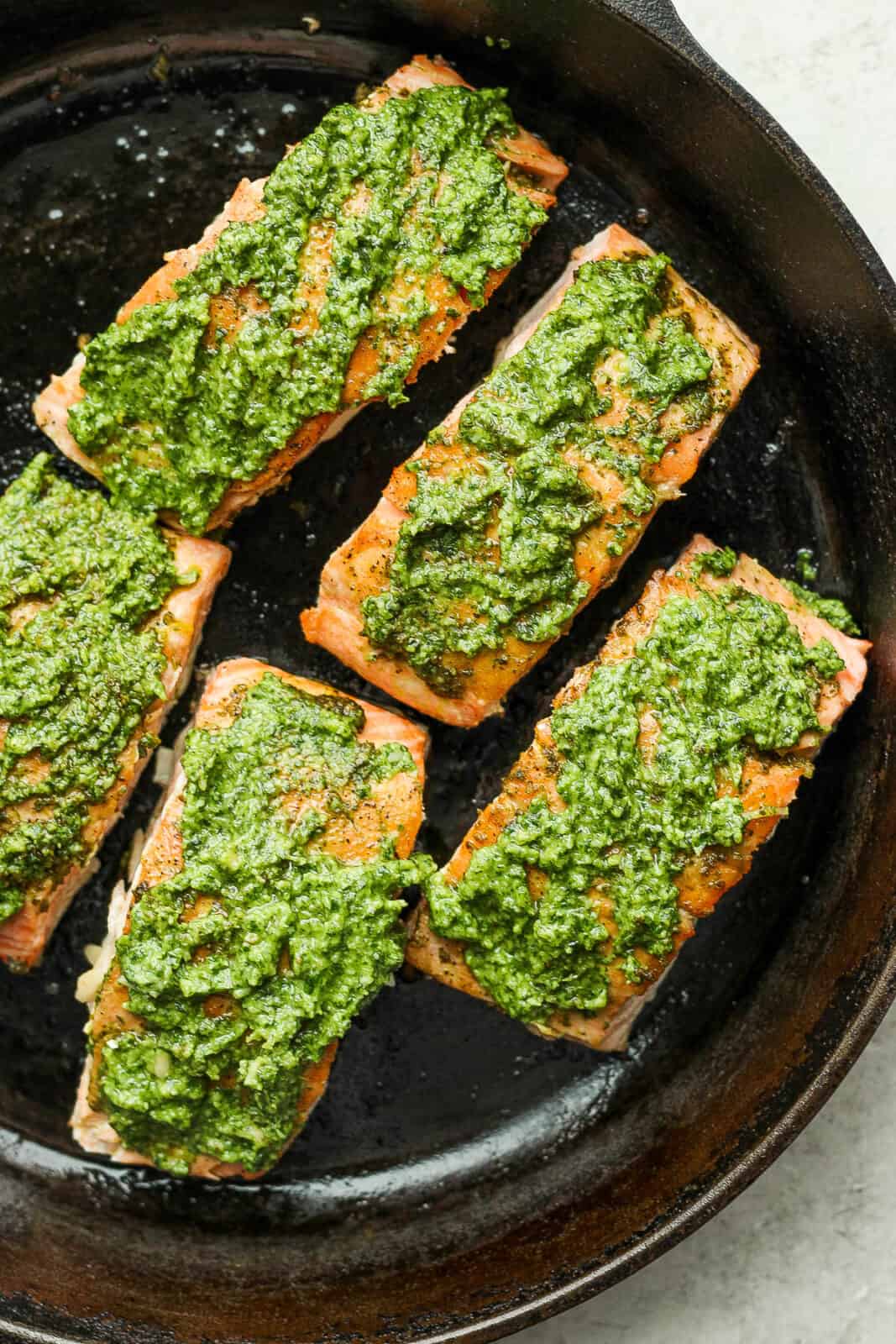 Pesto salmon fillets in a cast iron skillet with more pesto added on top.