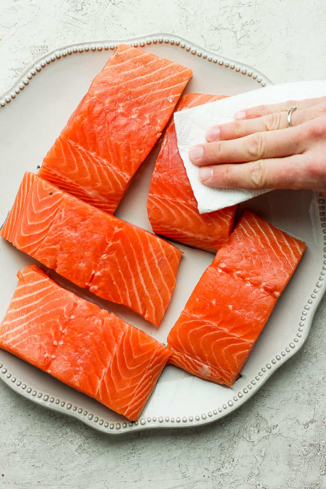 Salmon fillets being pat dry on a plate.