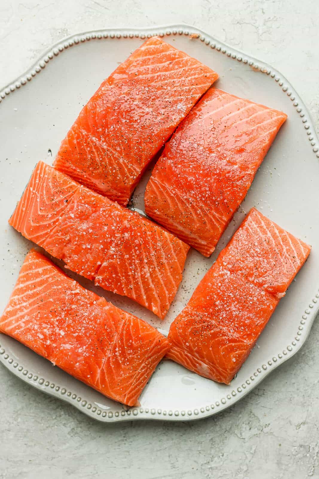 The salmon fillets seasoned with salt and pepper on a plate.