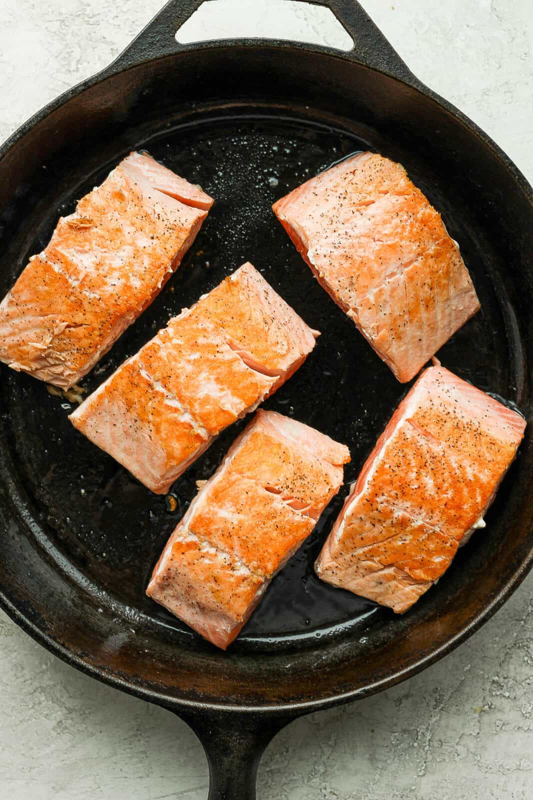 Salmon fillets being seared in a cast iron skillet.