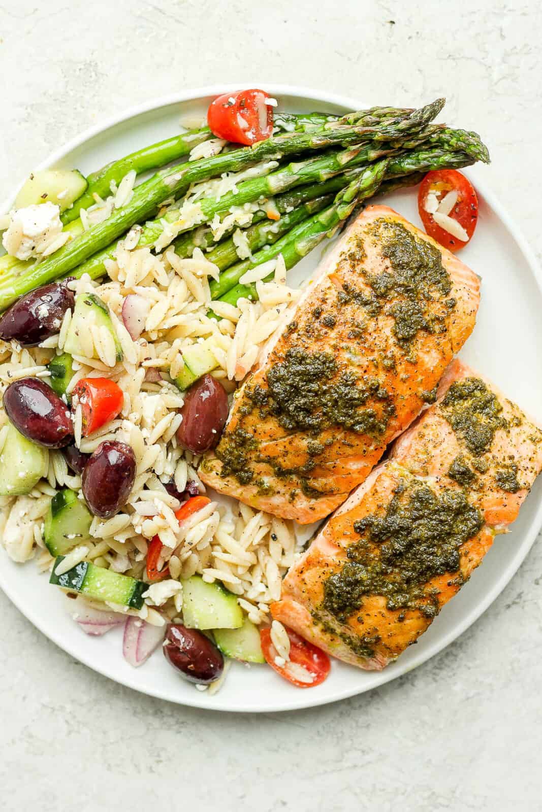 A simple pesto salmon on a plate with greek orzo salad and asparagus.