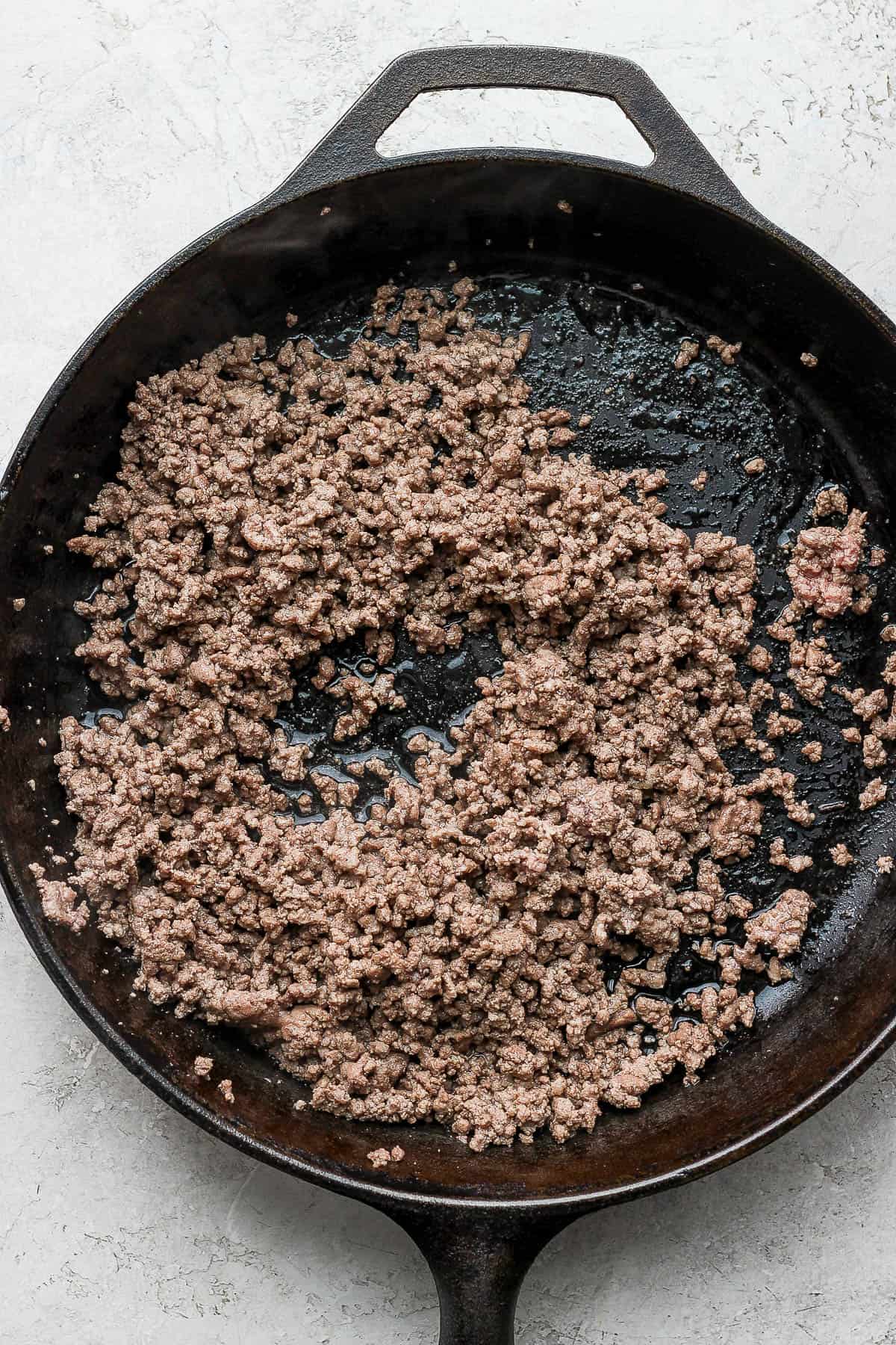 A pound of ground beef being browned in a cast iron skillet.