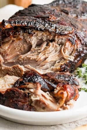 A pork shoulder roast on a platter with part of it shredded.