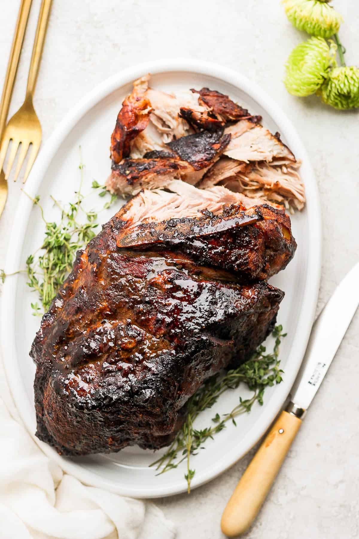 A pork shoulder roast on a platter that is starting to be shredded.