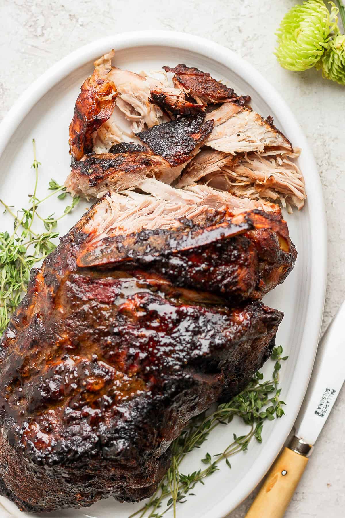 A partially shredded pork shoulder roast on a platter with a knife on the side.