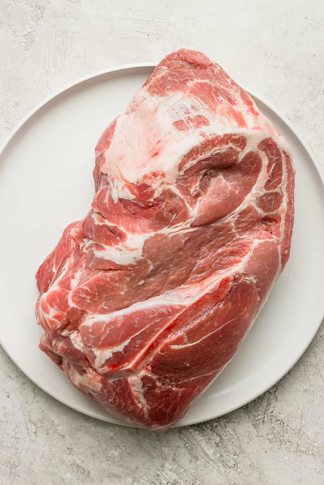 A raw bone-in pork shoulder on a plate.