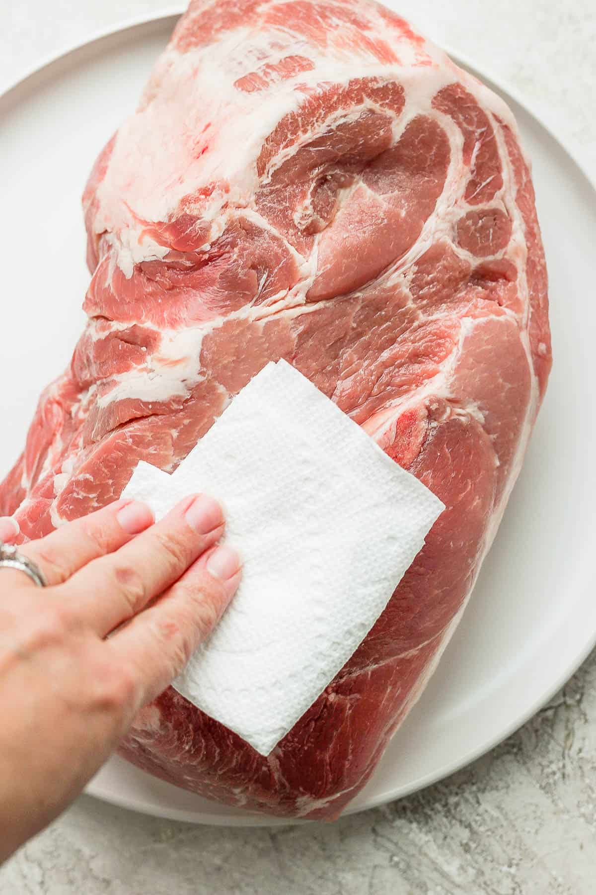 A pork shoulder being pat dry with a paper towel.
