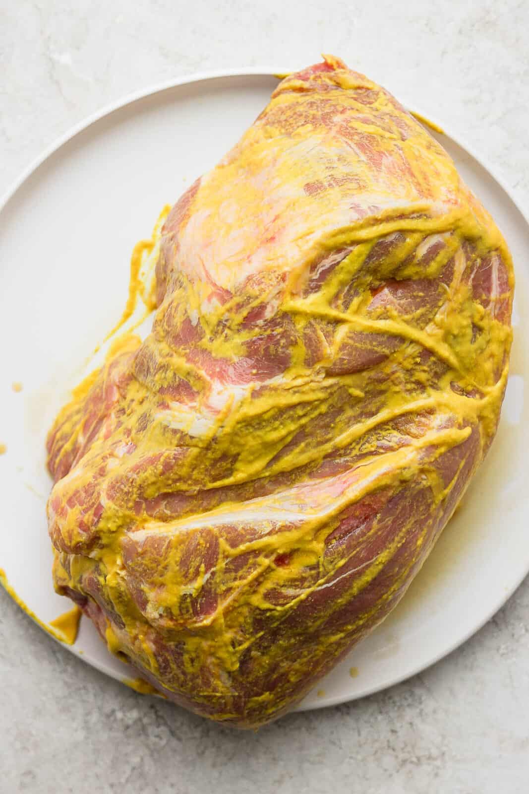 A pork shoulder with yellow mustard rubbed all over the outside.