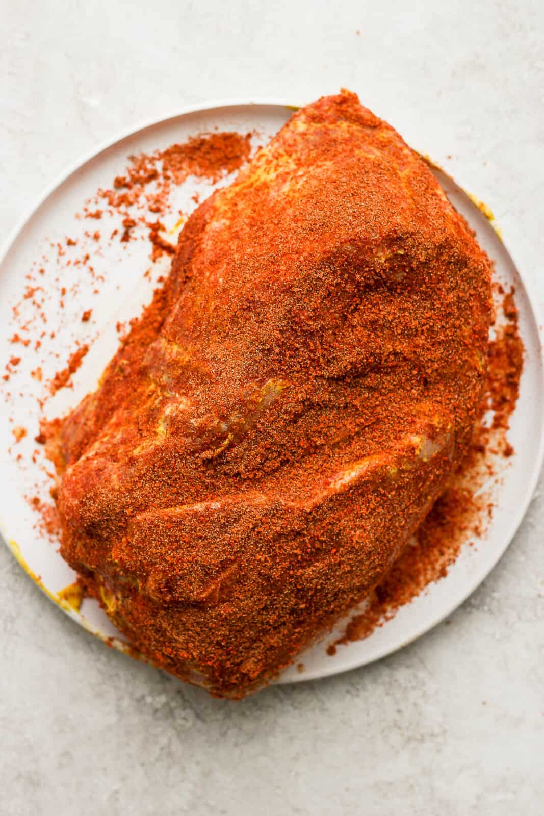 A pork shoulder coated with a homemade dry rub on a plate.