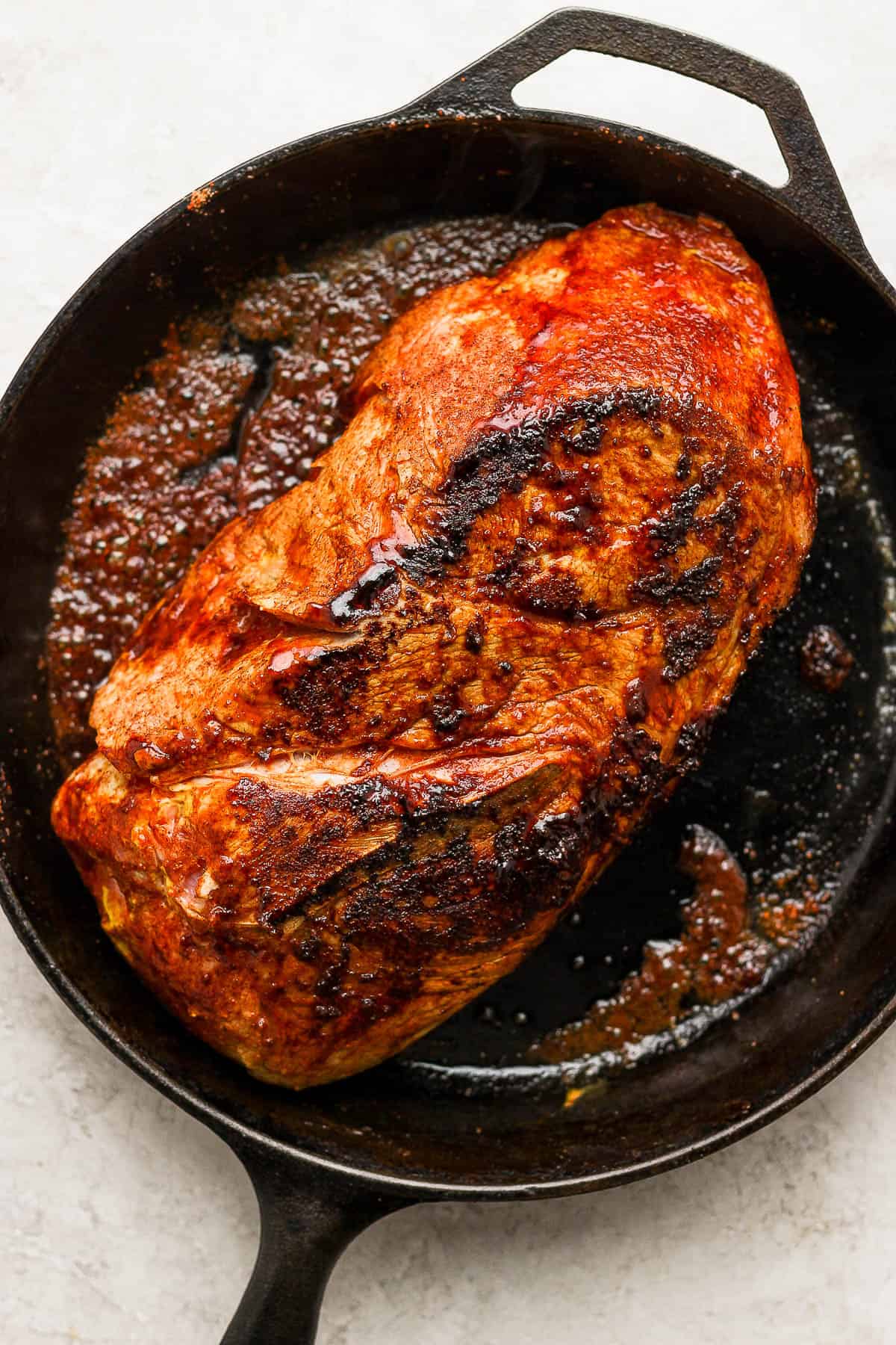 A pork shoulder being seared in a cast iron skillet.