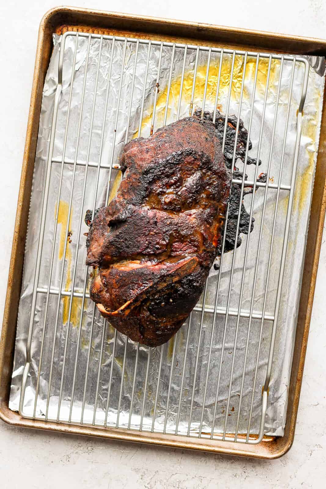 A pork shoulder roast on a wire rack which is on a foil-lined baking sheet.