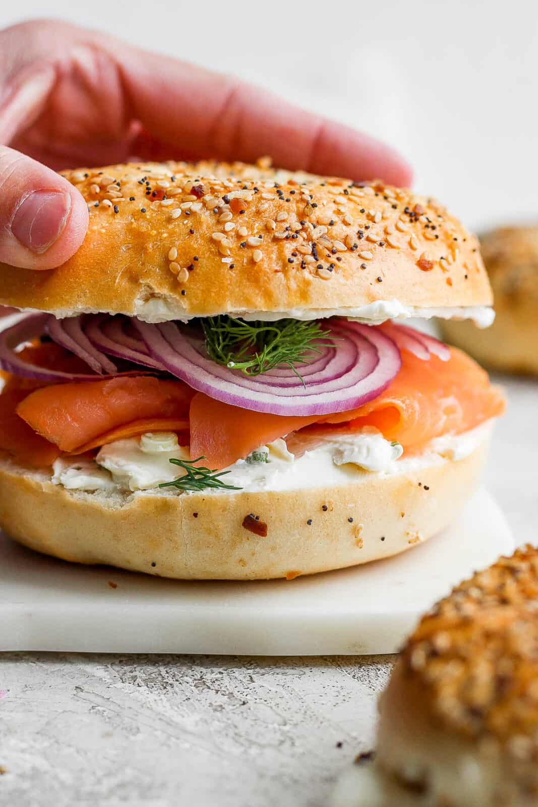 A hand placing the top half of a bagel on top.