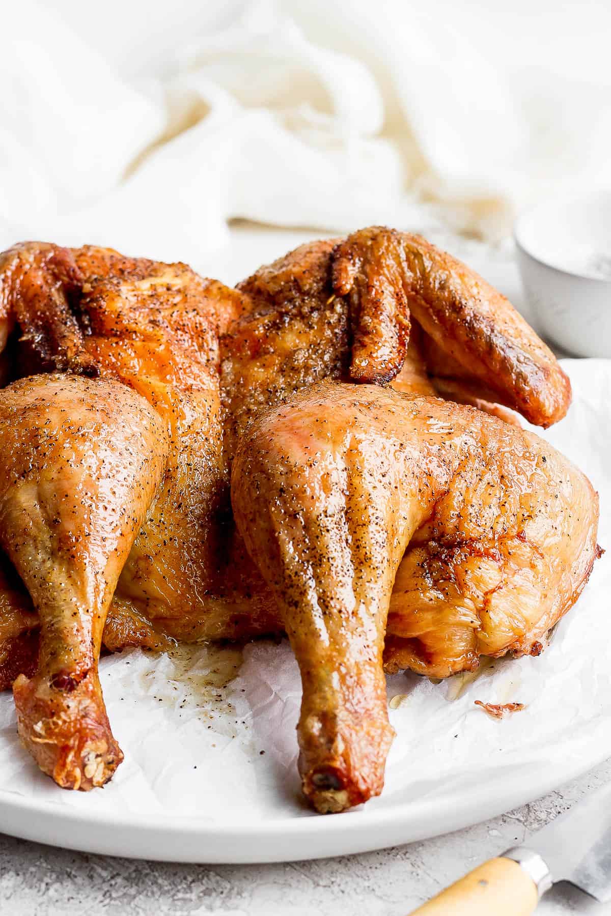 A smoked spatchcocked chicken on a plate, fully cooked, with a knife next to the plate.