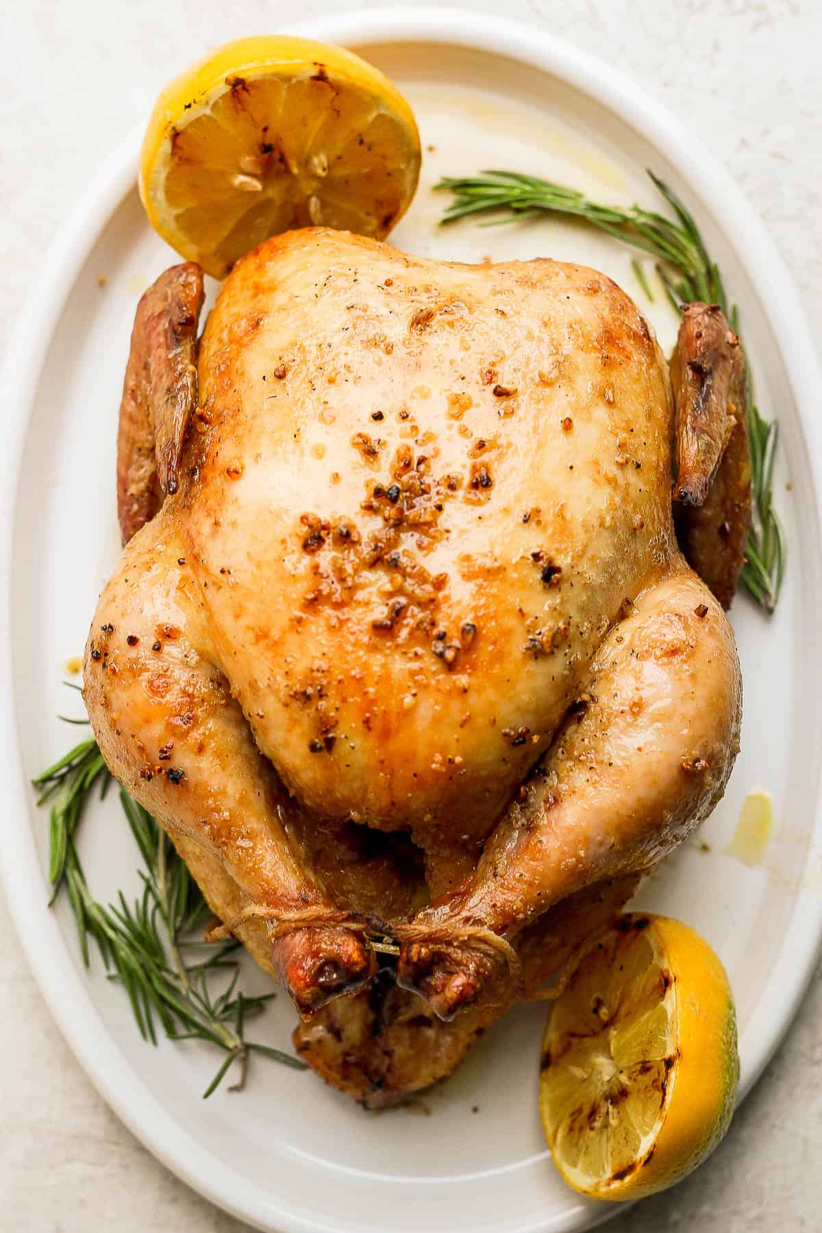 A whole smoked chicken on a platter with rosemary and lemon. 