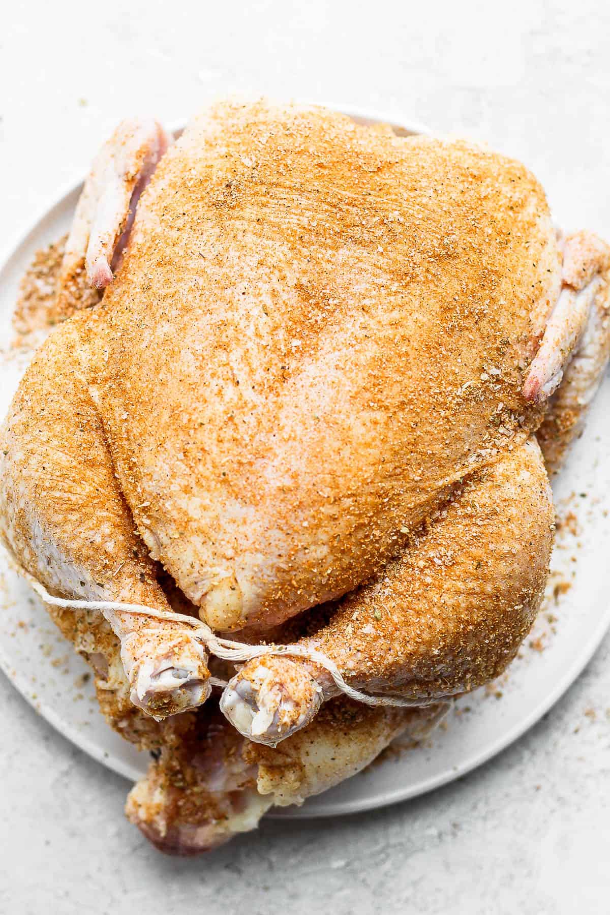 A whole, raw chicken covered in dry rub. 