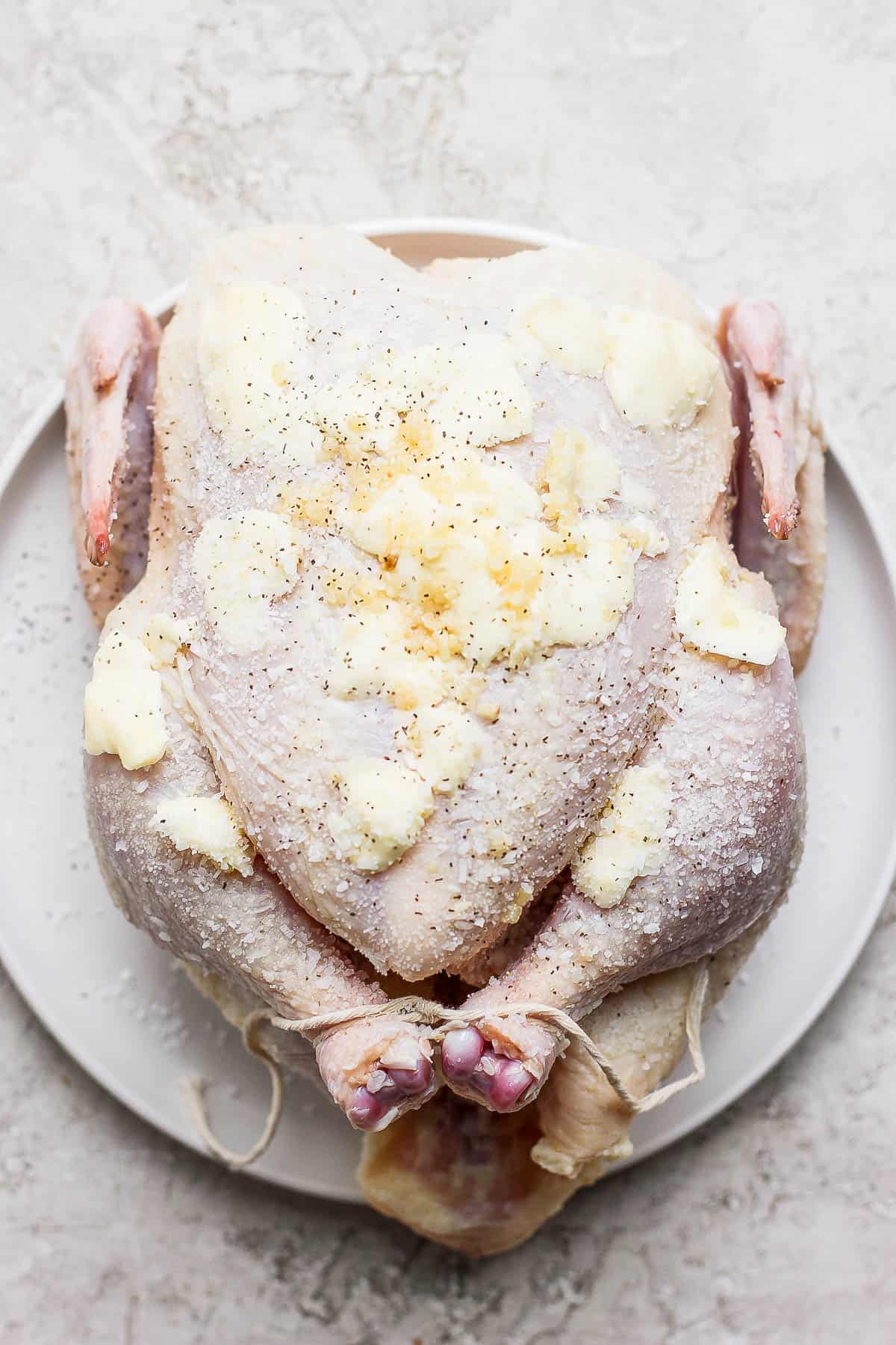A whole, raw chicken covered in butter and garlic. 