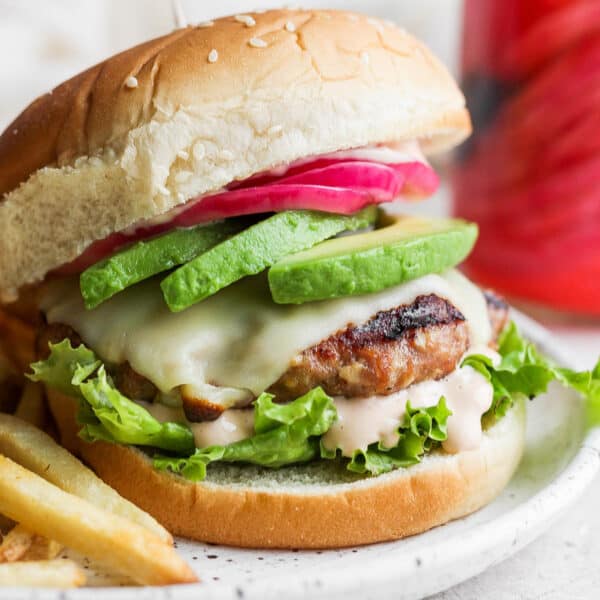 Avocado turkey burger on a bun on a plate with fried.