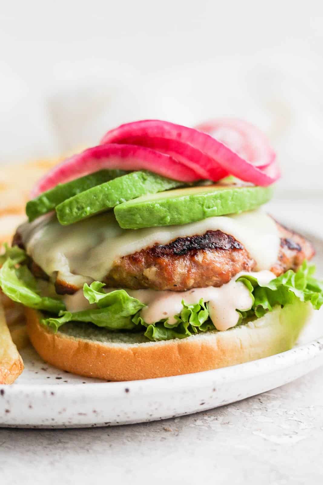An avocado turkey burger on a bun with lettuce, burger sauce, avocado, and pickled onions.