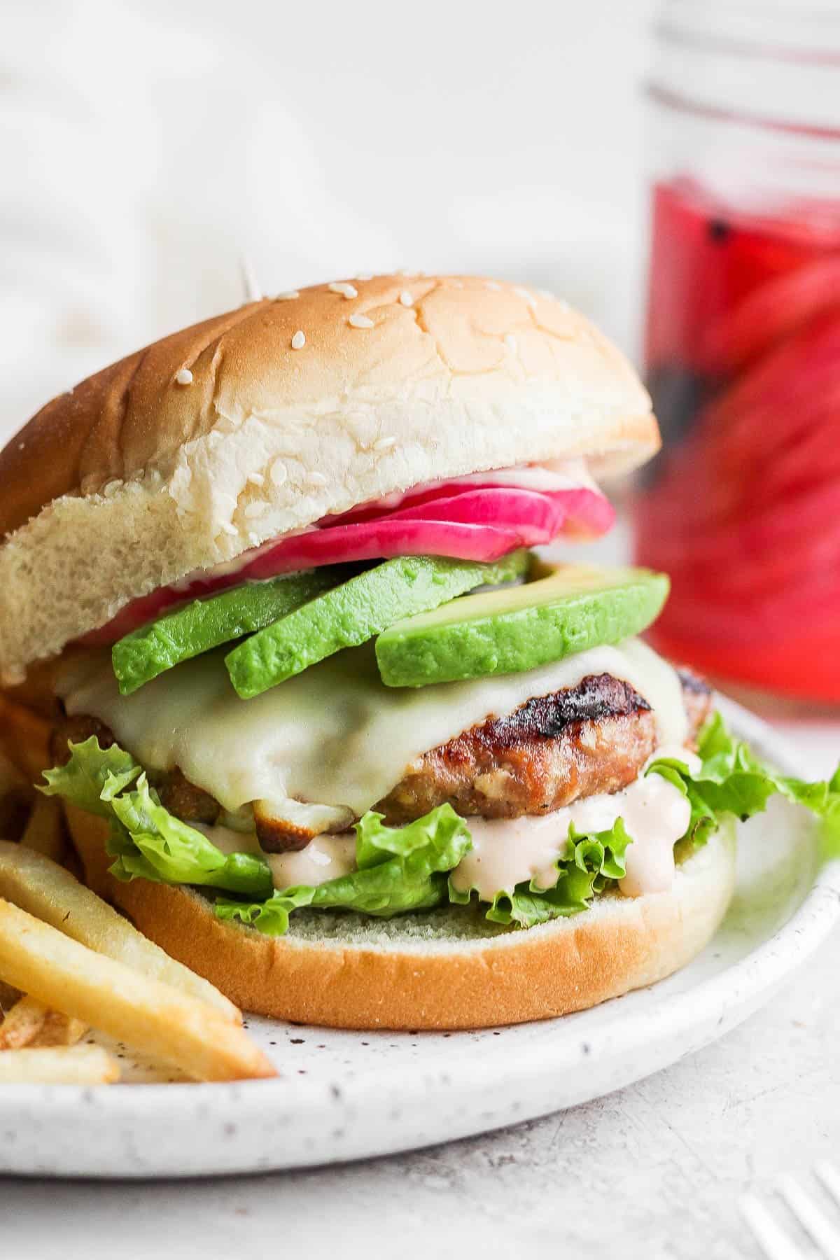 A turkey burger on a bun with avocado and pickled onions.