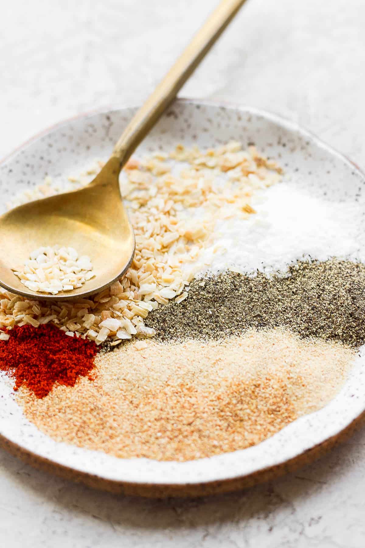 Burger seasoning ingredients in a bowl with a golden spoon. 