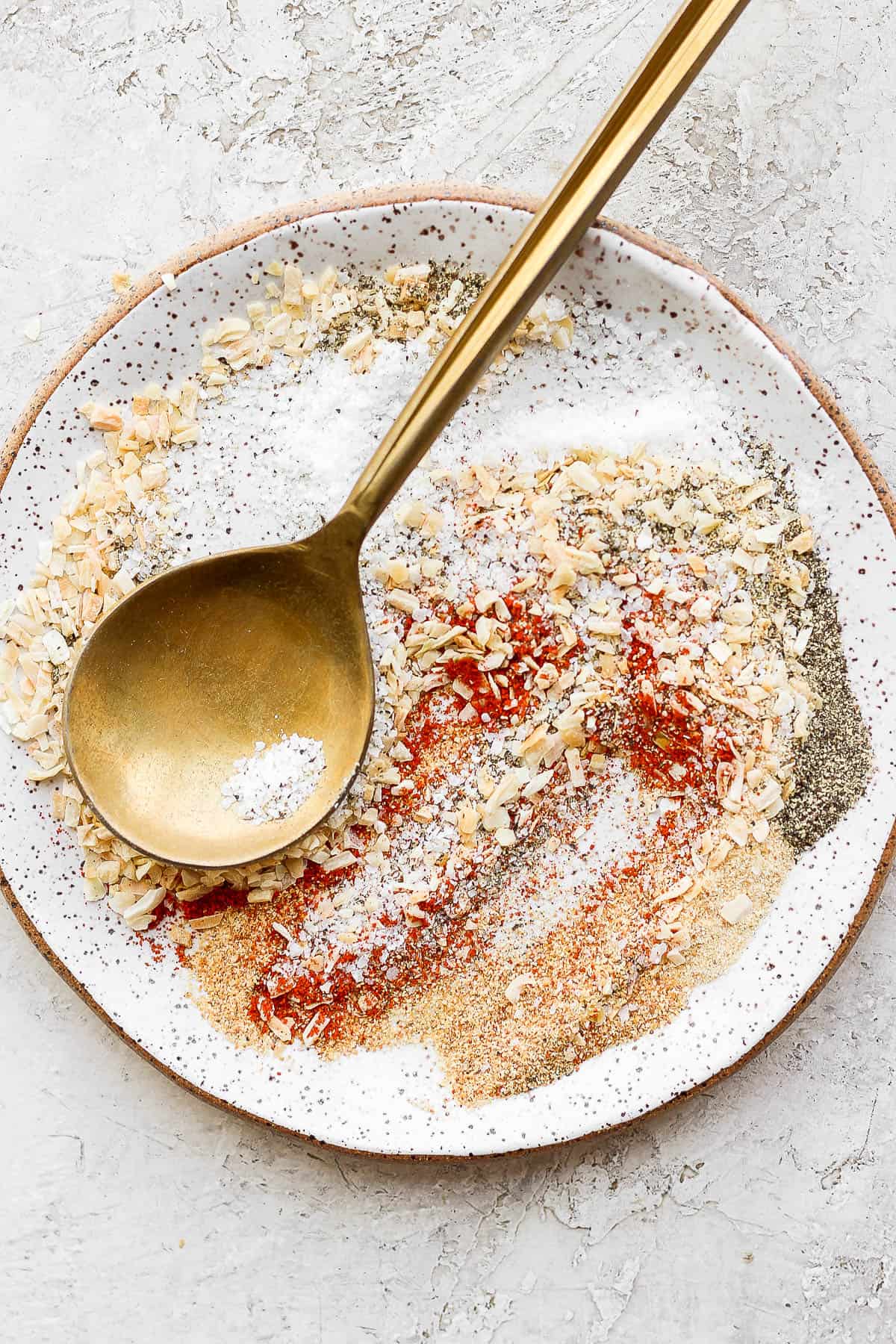 All of the seasoning ingredients mixed in a bowl with a golden spoon. 