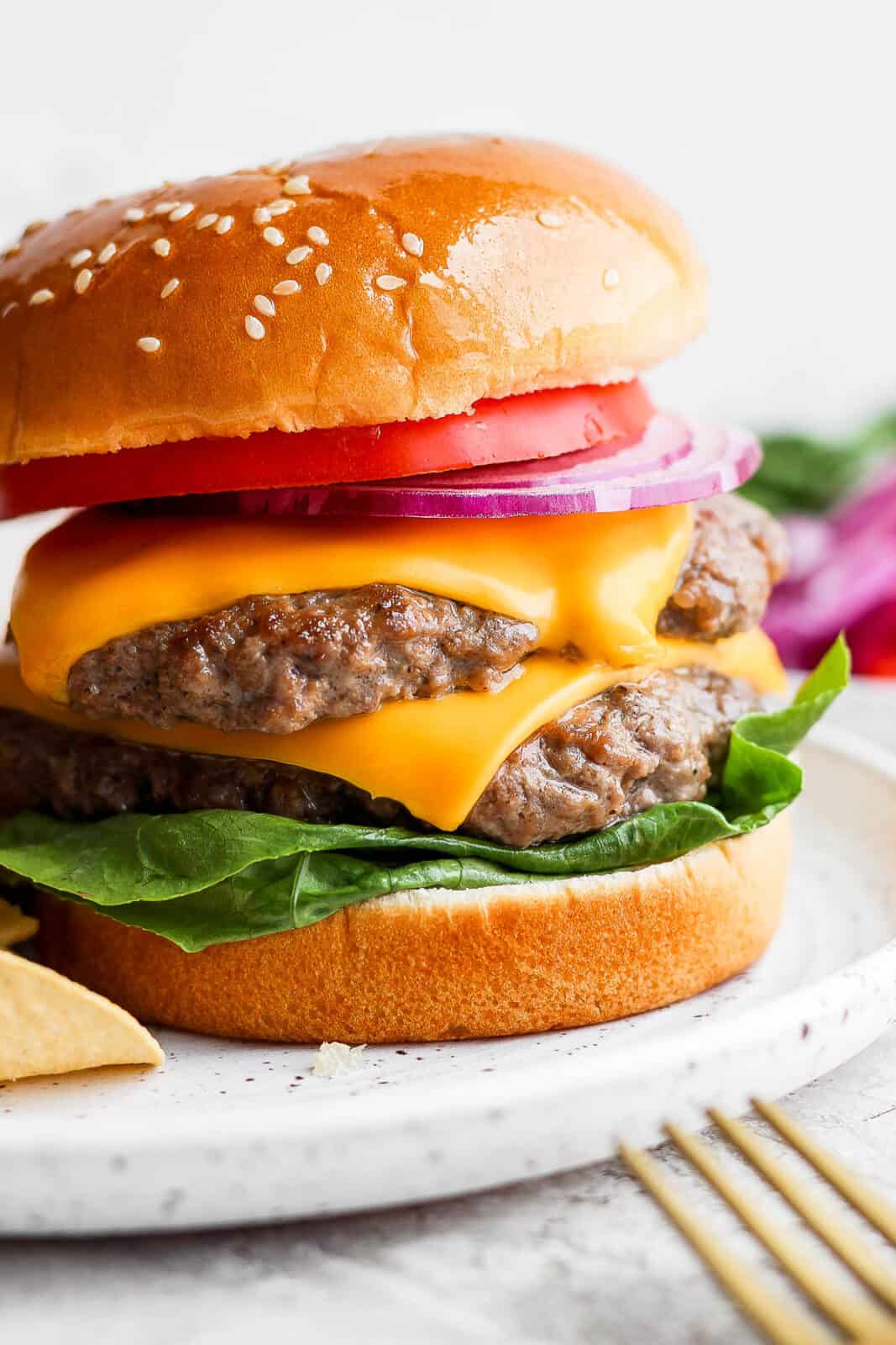 Two butter burgers on a bun with cheese, lettuce, onion and tomato. 