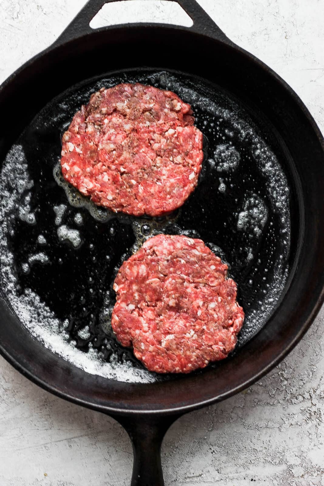 Two burger patties inside the cast iron skillet. 