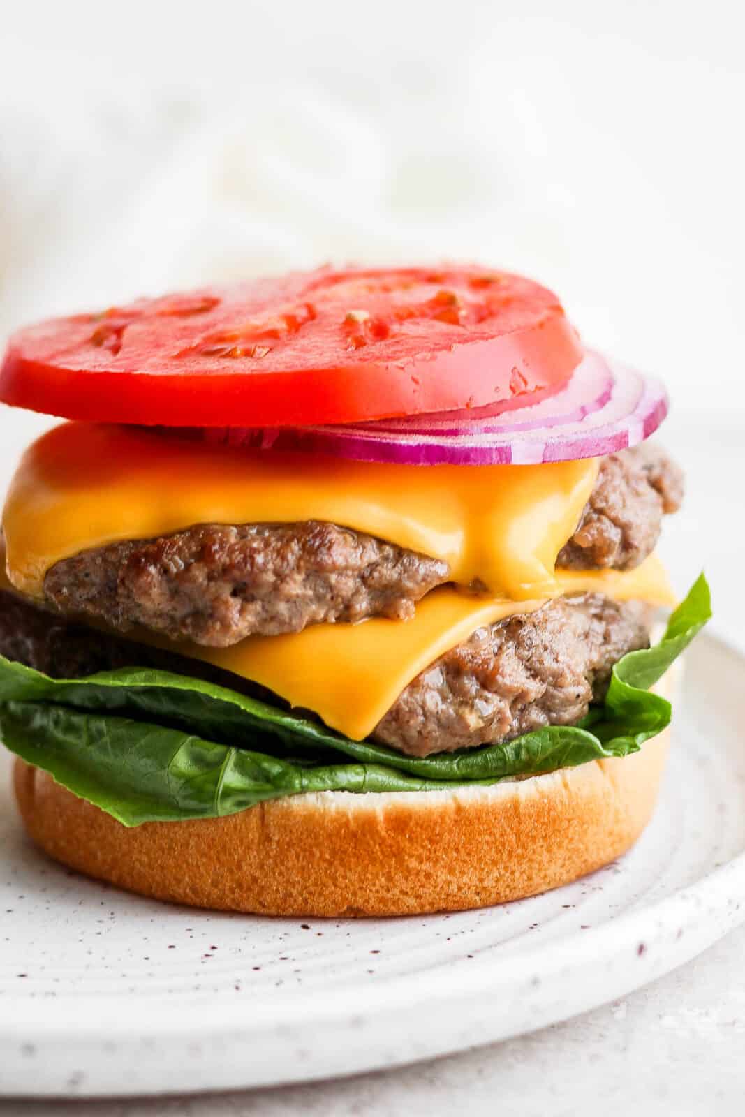 Two butter burgers on a bottom bun with onion and tomato. 