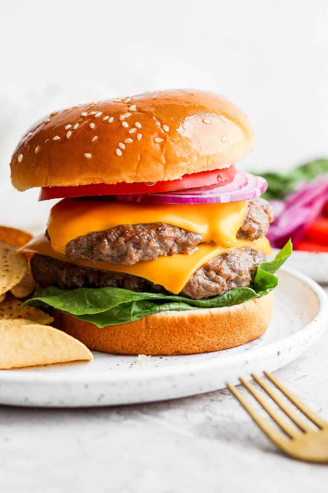 A double butter burger cheeseburger on a bun with lettuce, tomato and onion. 