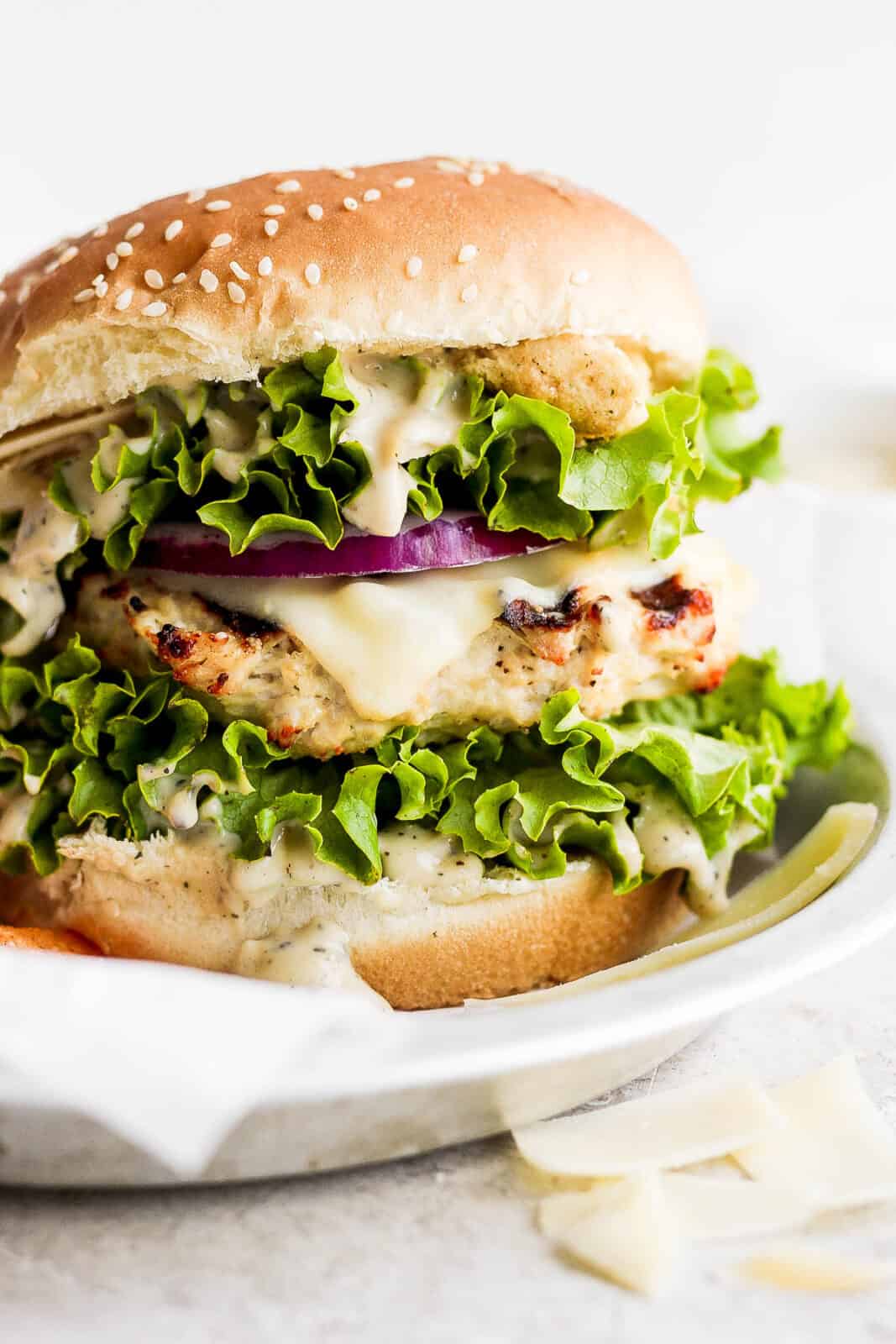 A chicken caesar burger on a bun with all the toppings.