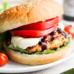 A caprese burger with a bun, chicken burger, mozzarella, basil, tomato and balsamic glaze.