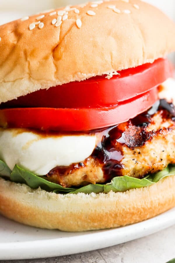A caprese burger with a bun, chicken burger, mozzarella, basil, tomato and balsamic glaze.