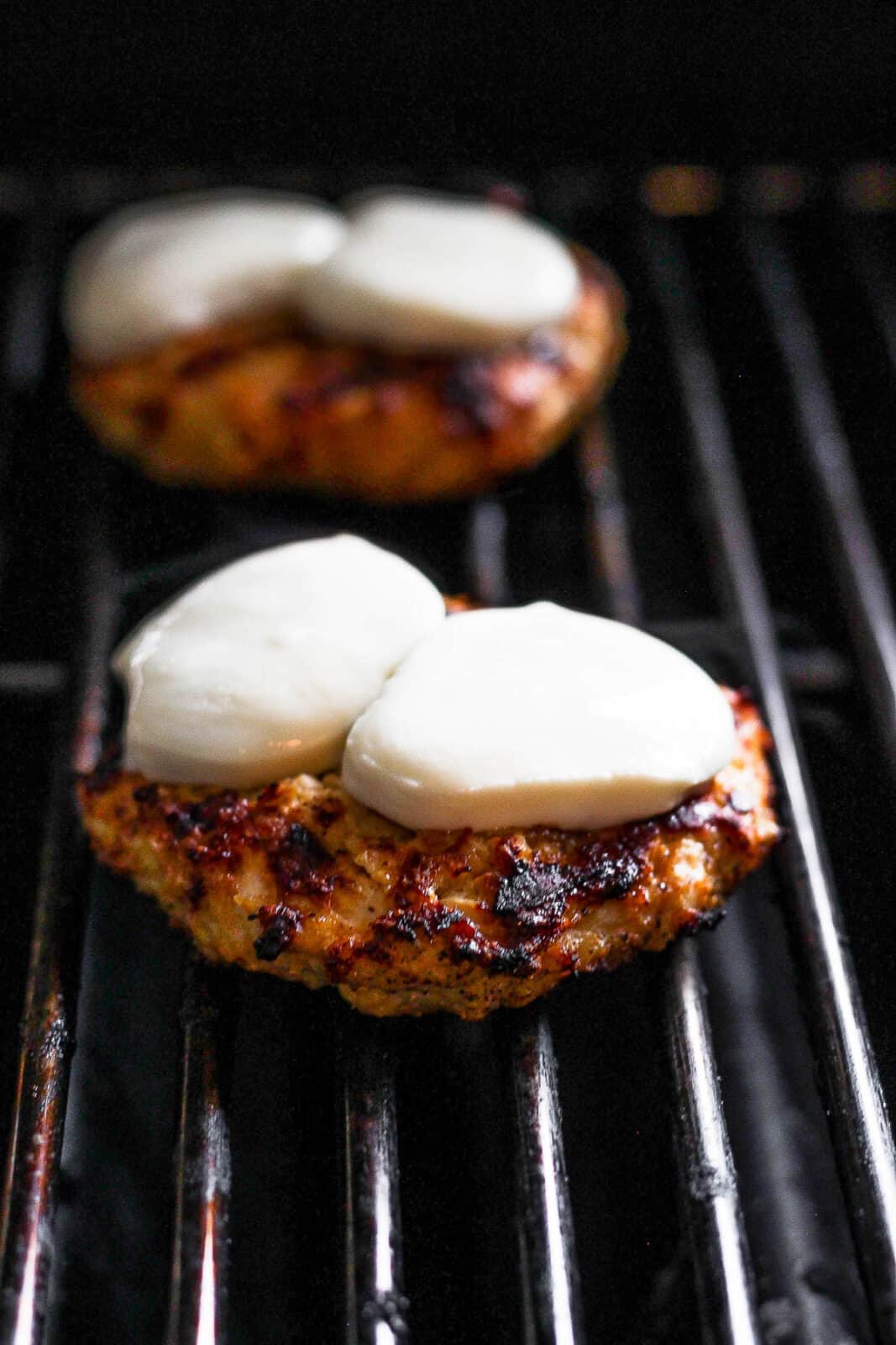 Chicken burgers on the grill with fresh mozzarella slices on top. 