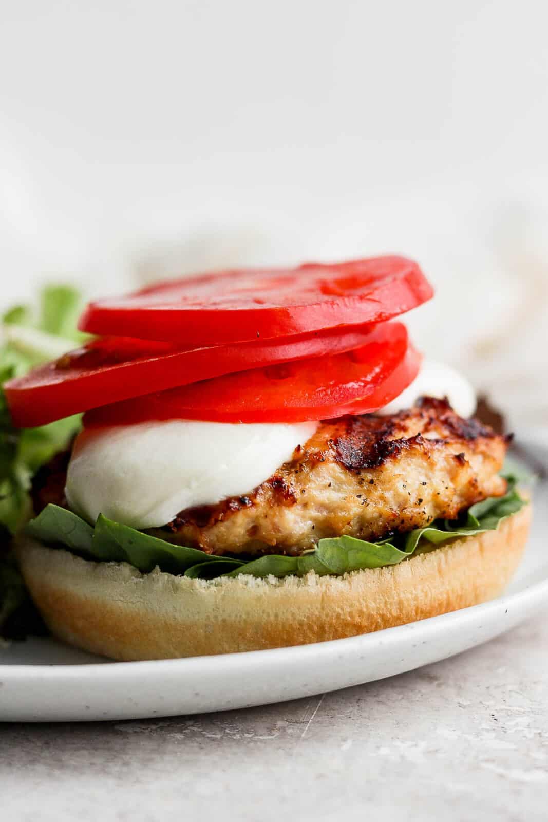 A caprese burger on a bun with tomato and basil. 